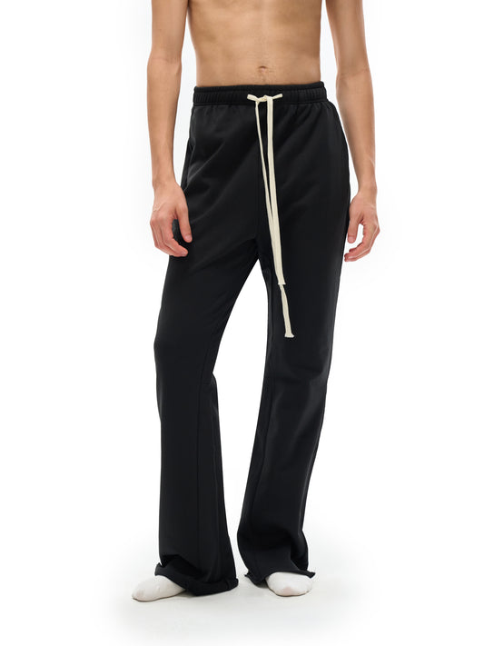 Lower half of model wearing the sustainable 420 GSM Future-Homme daily uniform mid rise flared cotton sweatpants in black front side on a white background