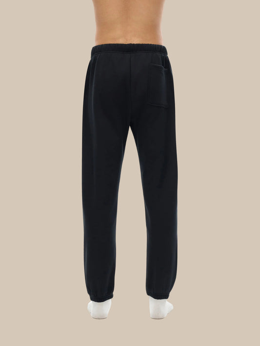 A Future-Homme model wearing the Fleece Please sweatpants in black showing the backside on a white background.