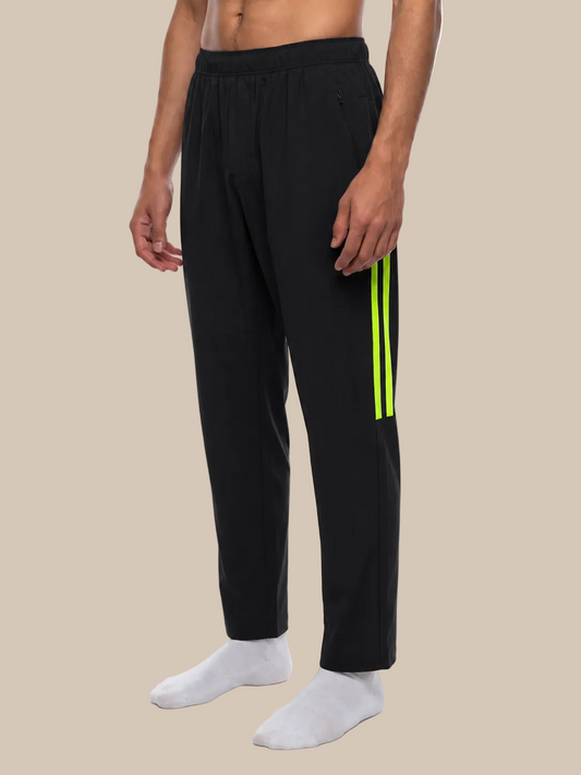Black jogger pants with green stripes worn by a person on a beige background