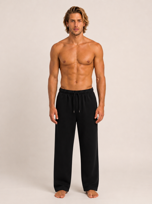 A shirtless male model stands against a plain light beige studio background wearing black drawstring lounge pants.