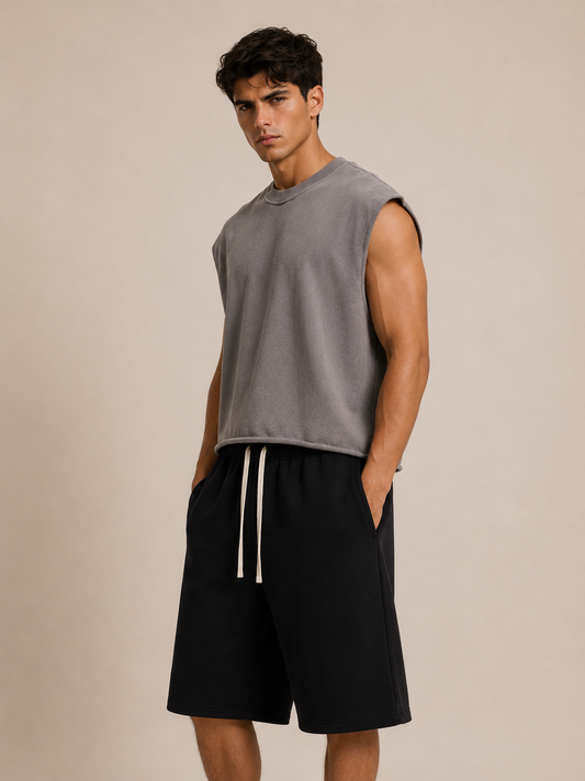 A man modeling a sleeveless gray crewneck sweatshirt and black drawstring shorts against a plain beige studio background.