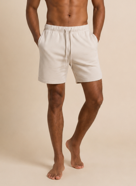 A man wearing off-white drawstring shorts, shown from the waist down against a solid beige studio background.