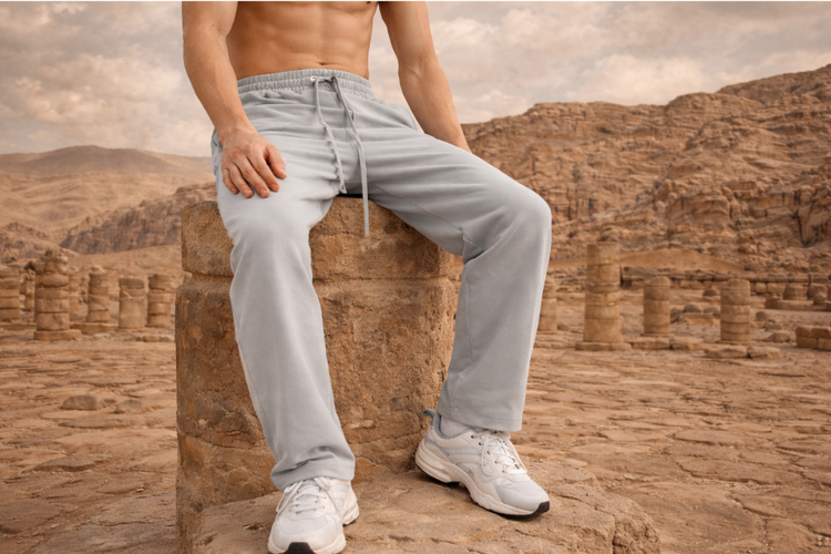 lower half of a male wearing gray sweatpants and white sneakers sitting on an ancient ruin column