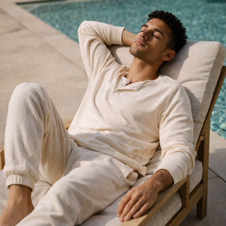 A male lounging poolside in a cream colored top and bottom. 