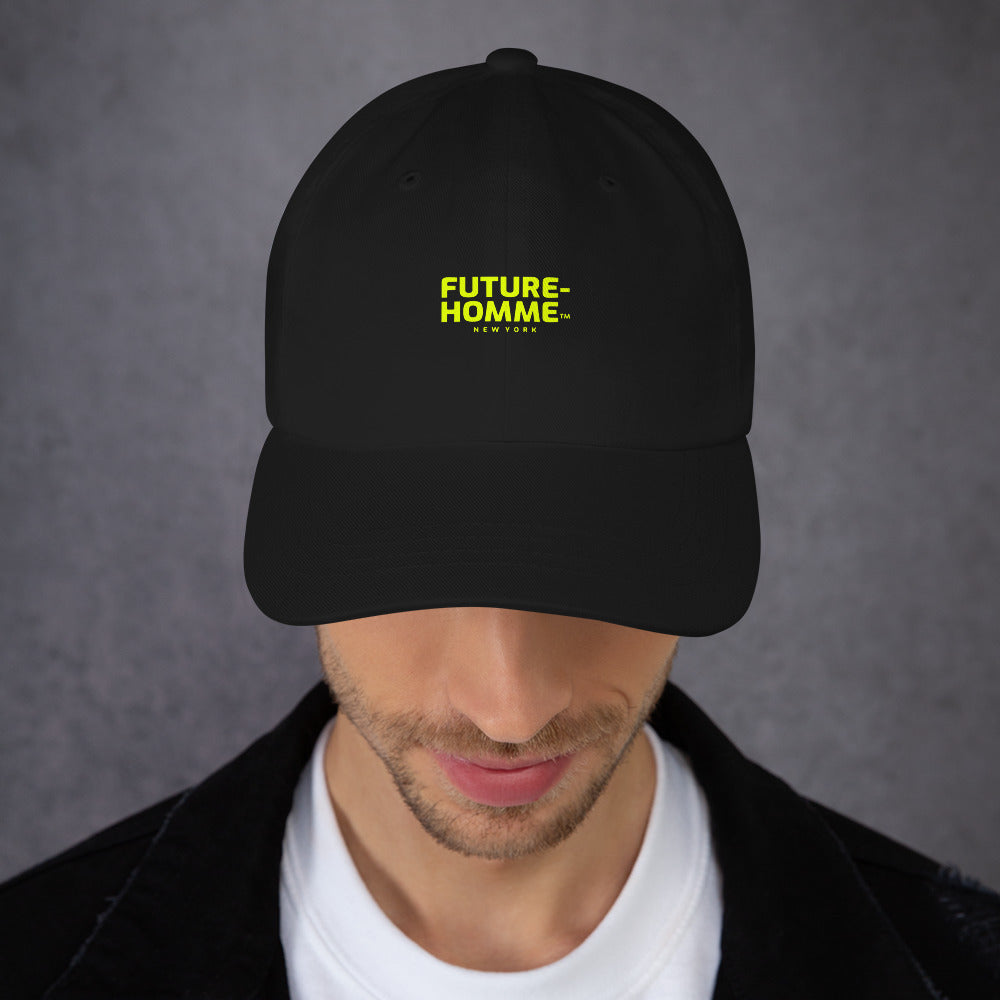 Male model wearing a black baseball cap with yellow Future-Homme logo on a gray background. 