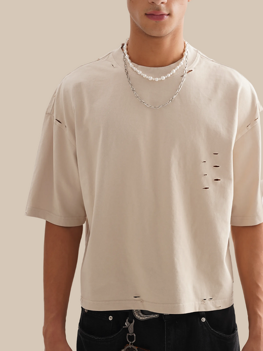 Beige t-shirt with distressed details worn by a person on a white background