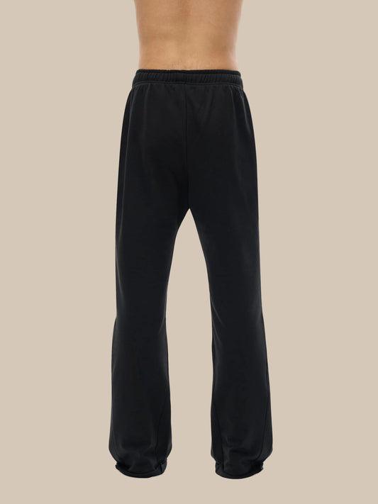 Lower half of model wearing the sustainable 420 GSM Future-Homme daily uniform mid rise flared cotton sweatpants in black back side on a white background