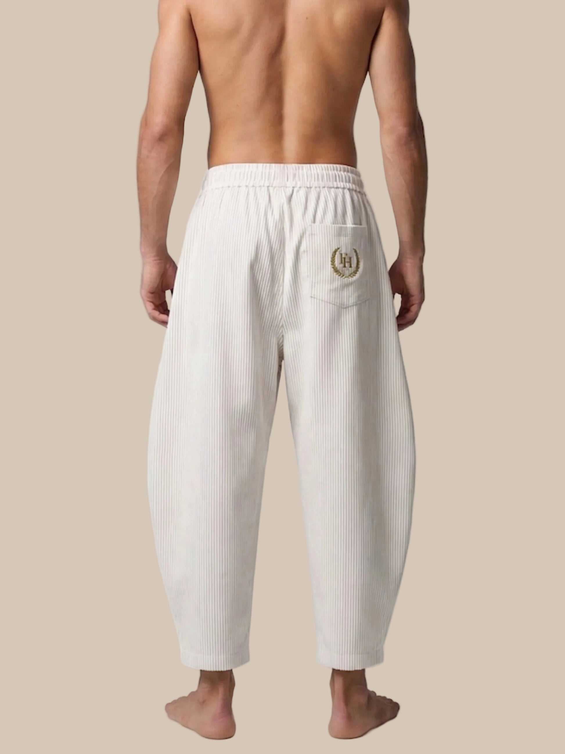 Person wearing white ribbed pants with a logo on a white background