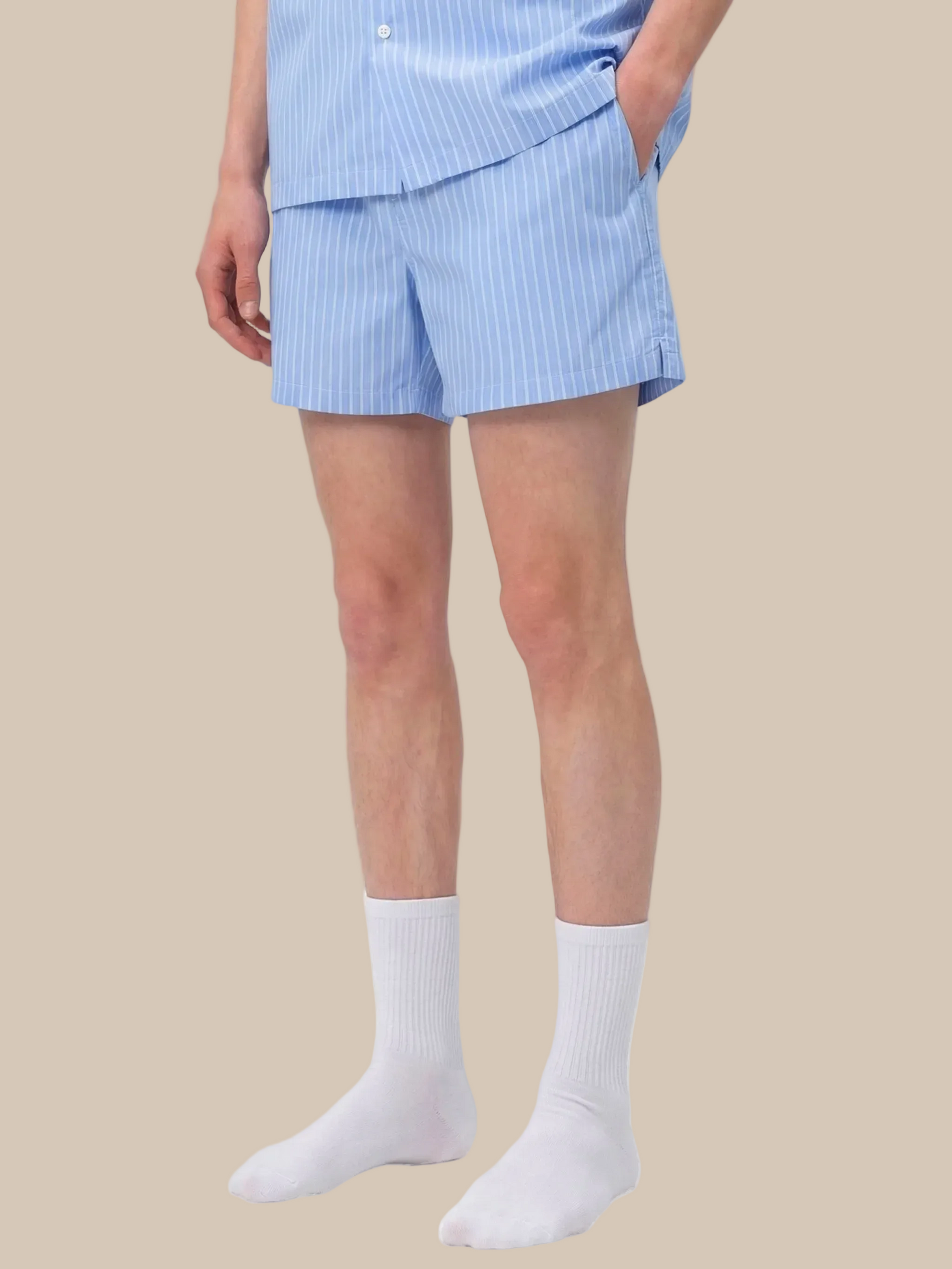 Person wearing light blue striped pajama shorts and white socks on a white background