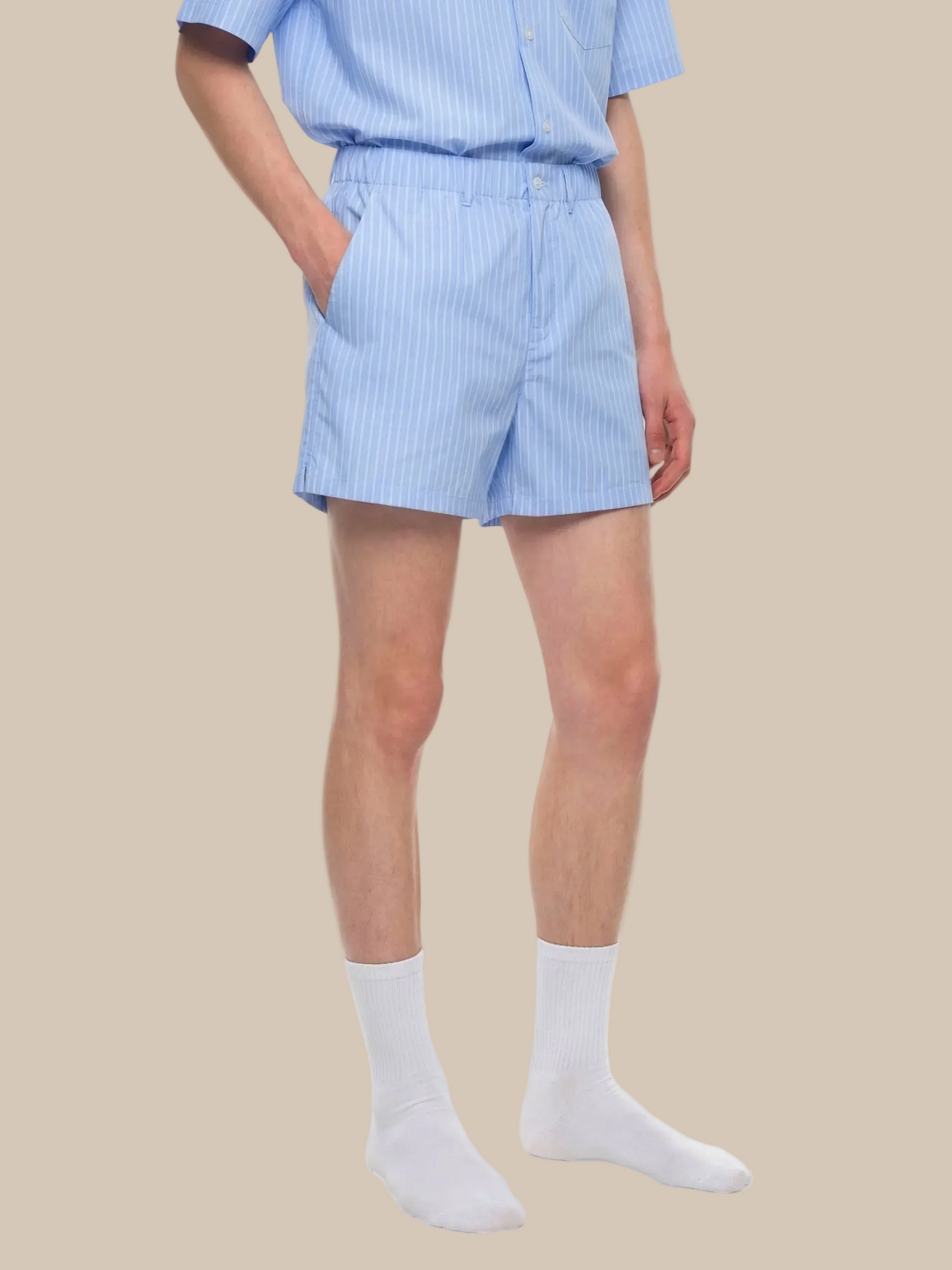 Person wearing a light blue striped shirt and shorts with white socks on a white background