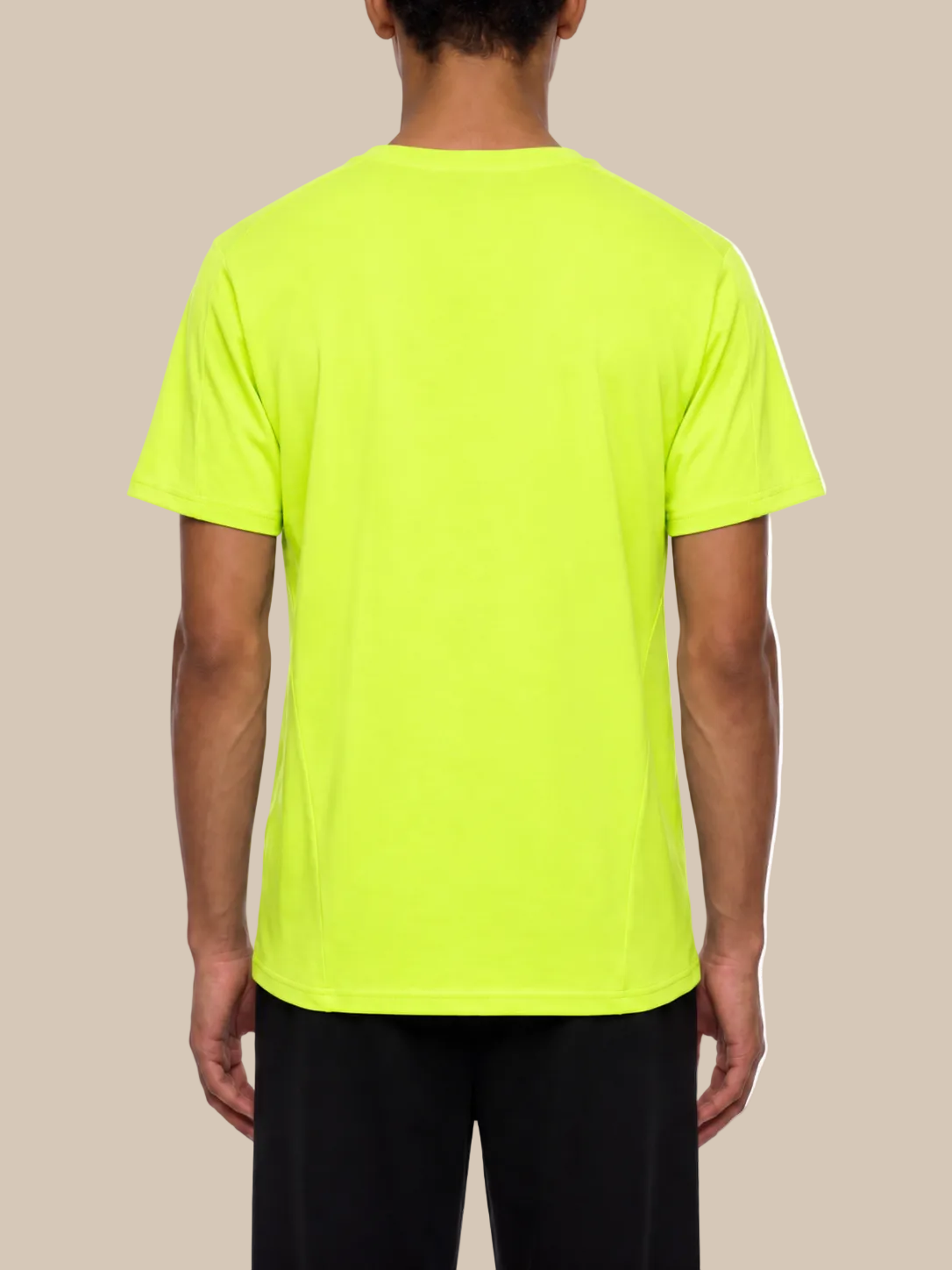 Backside of a person wearing a bright green performance t-shirt on a beige background. 