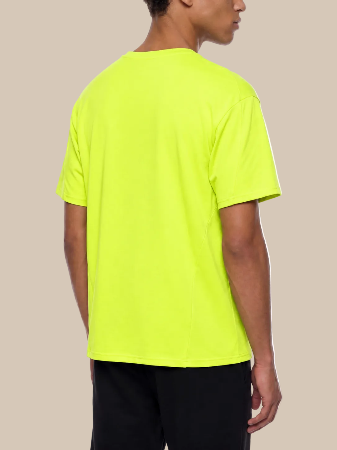 Backside of a person wearing a bright green performance t-shirt on a beige background. 