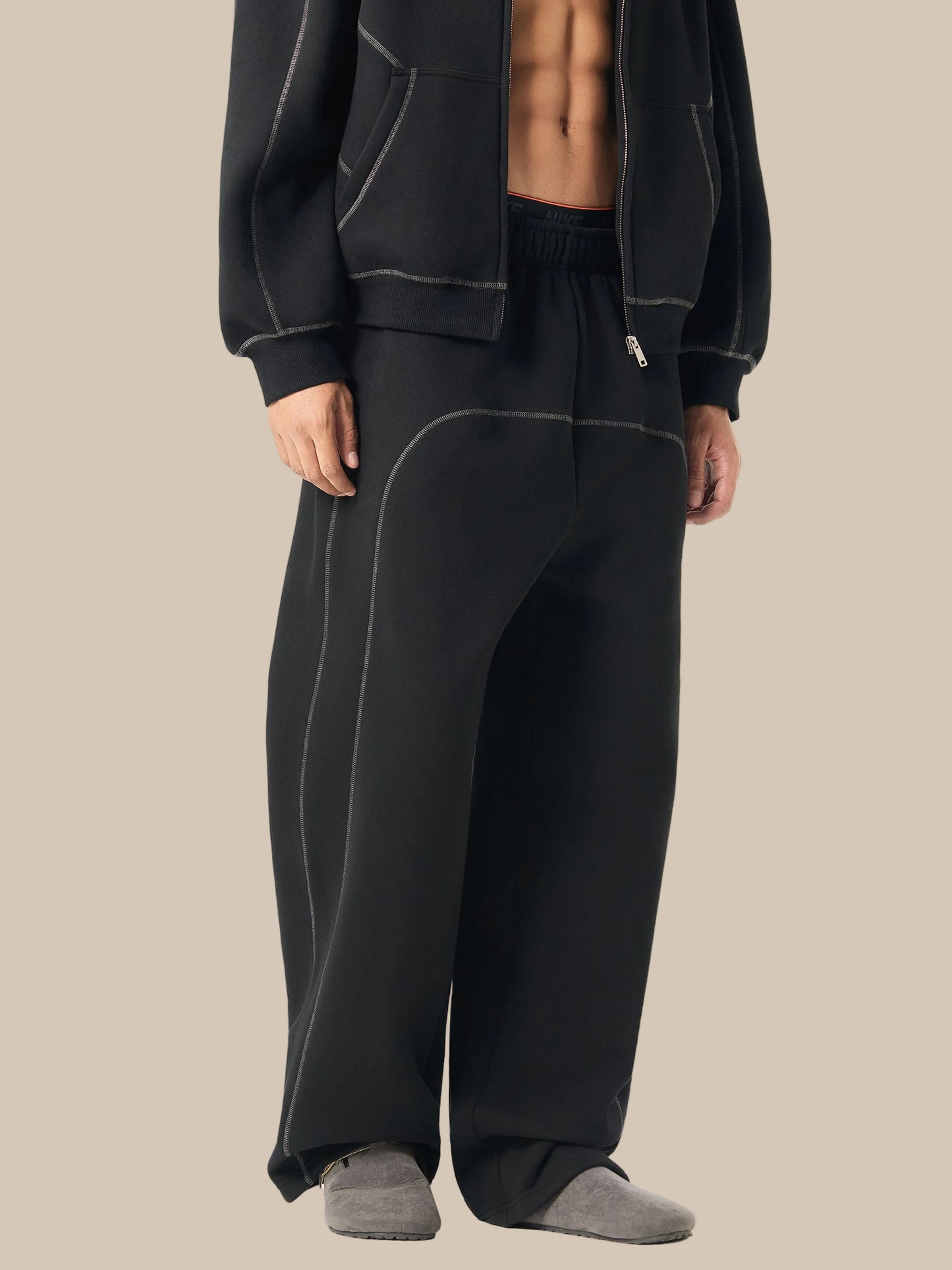 Person wearing black tracksuit pants and jacket on a white background