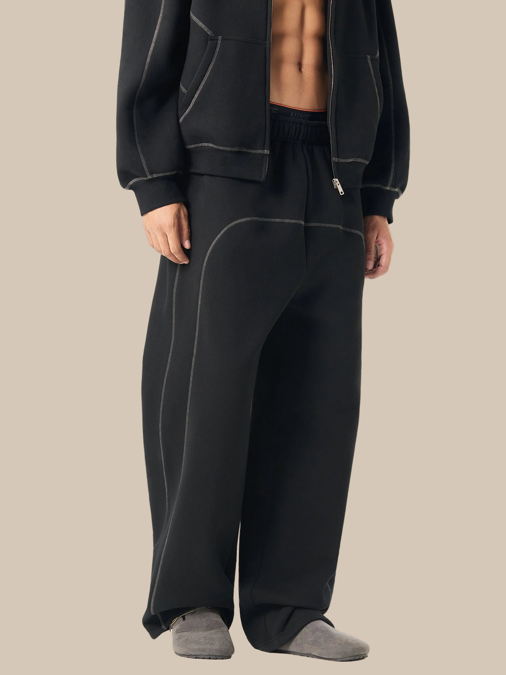 Person wearing black tracksuit pants and jacket on a white background