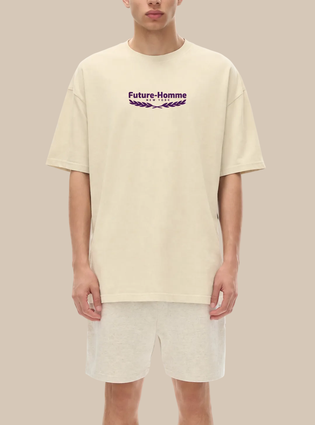 A person wearing a beige t-shirt with a future-homme logo with laurel on a white background. 