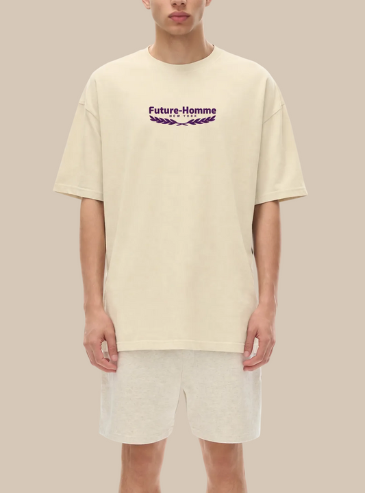 A person wearing a beige t-shirt with a future-homme logo with laurel on a white background. 