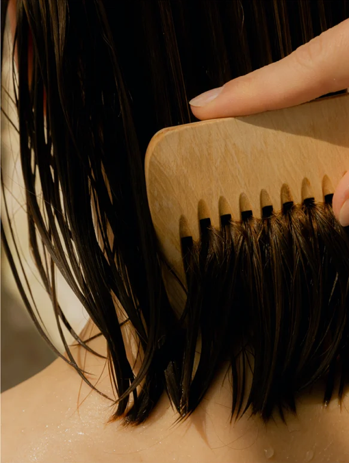 Person brushing their hair with a wooden comb