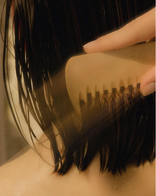 Close-up of a hand combing though dark hair.