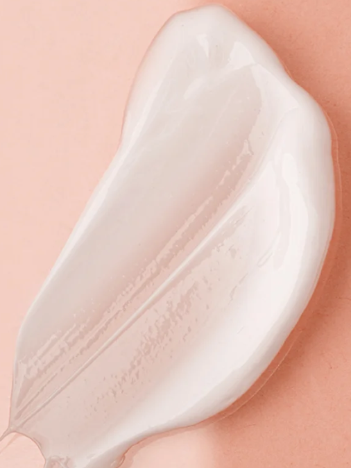 A white smear of product on a  pink background. 
