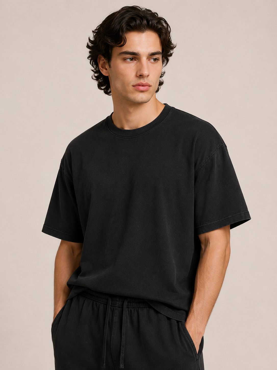 A man wearing a black short-sleeve crewneck t-shirt and black drawstring sweatpants, standing against a solid beige studio background.