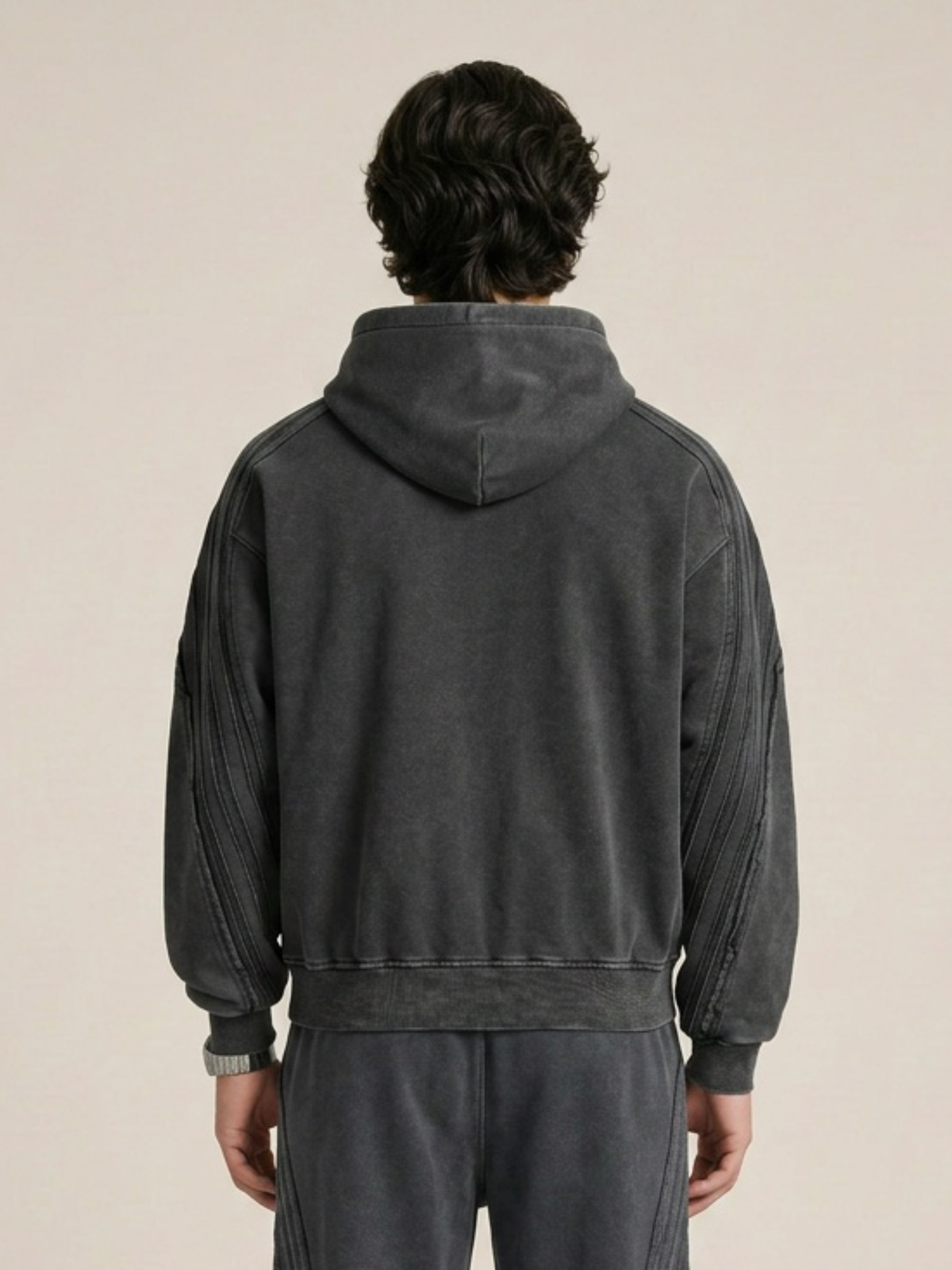 Backside of a model wearing a sun bleached deconstructed black hoodie with matching sweatpants on a beige background. 
