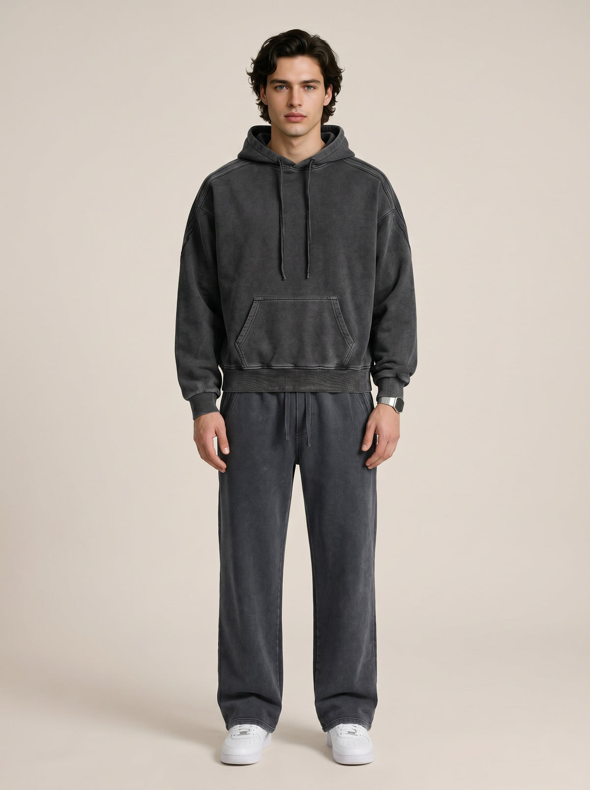 A model wearing a sun bleached deconstructed black hoodie with matching sweatpants on a beige background. 