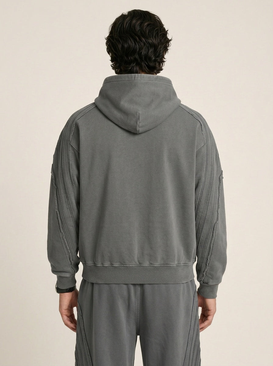 Up close backside of a model wearing a sun bleached deconstructed dark gray hoodie on a beige background. 