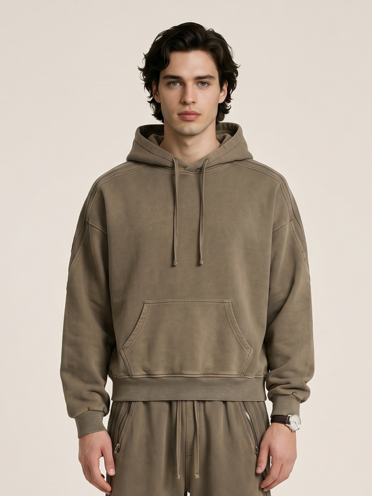 A model wearing a sun bleached deconstructed khaki hoodie with matching sweatpants on a beige background. 