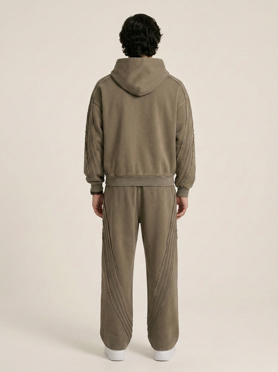 Backside of a model wearing a sun bleached deconstructed khaki hoodie with matching sweatpants on a beige background. 