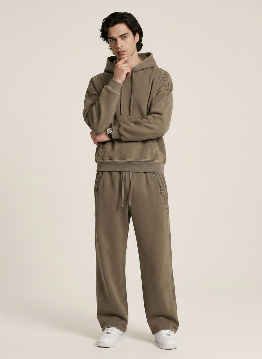 A model wearing a sun bleached deconstructed khaki hoodie with matching sweatpants on a beige background. 