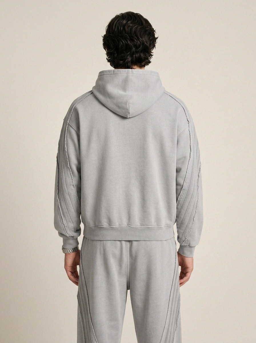 Backside of a model wearing a sun bleached deconstructed light gray hoodie and matching sweatpants on a beige background. 