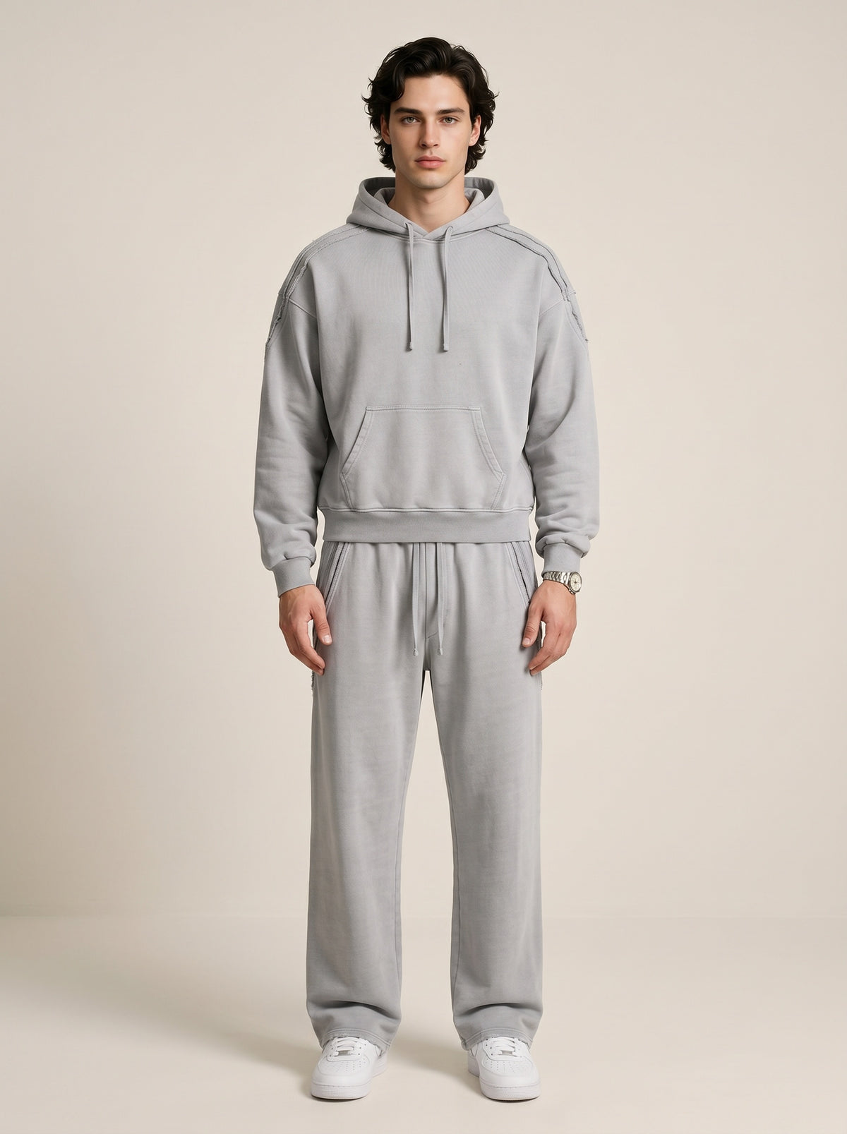 a model wearing a light gray sun bleached deconstructed hoodie with matching pants on a beige background. 
