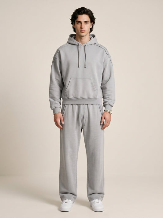 a model wearing a light gray sun bleached deconstructed hoodie with matching pants on a beige background. 