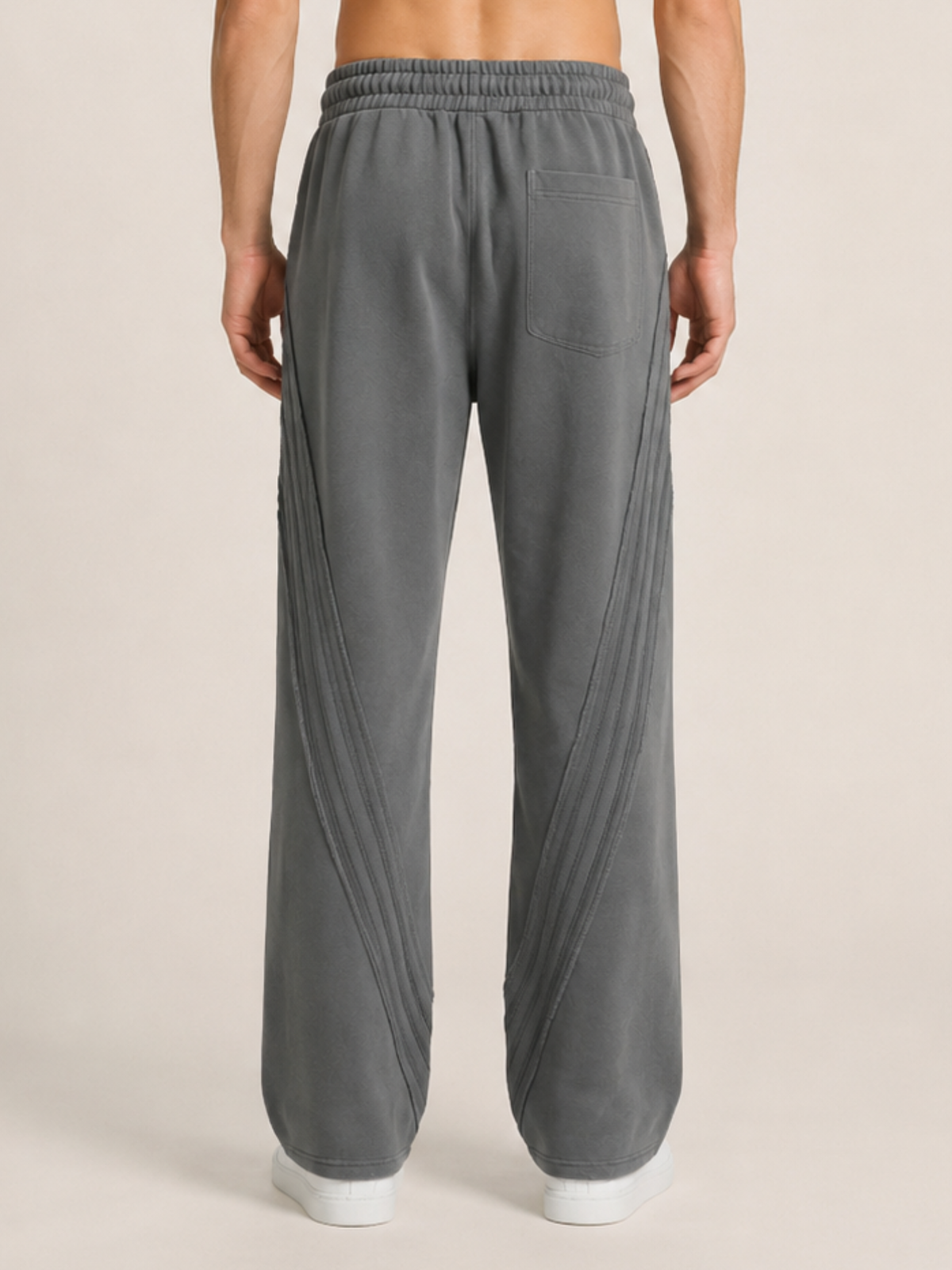 Backside close up shot of a model wearing a pair of dark gray sweatpants on a beige background. 