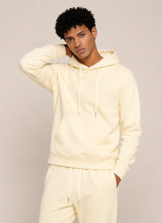A man modeling a cream-colored fleece hoodie and matching sweatpants against a light beige studio background.