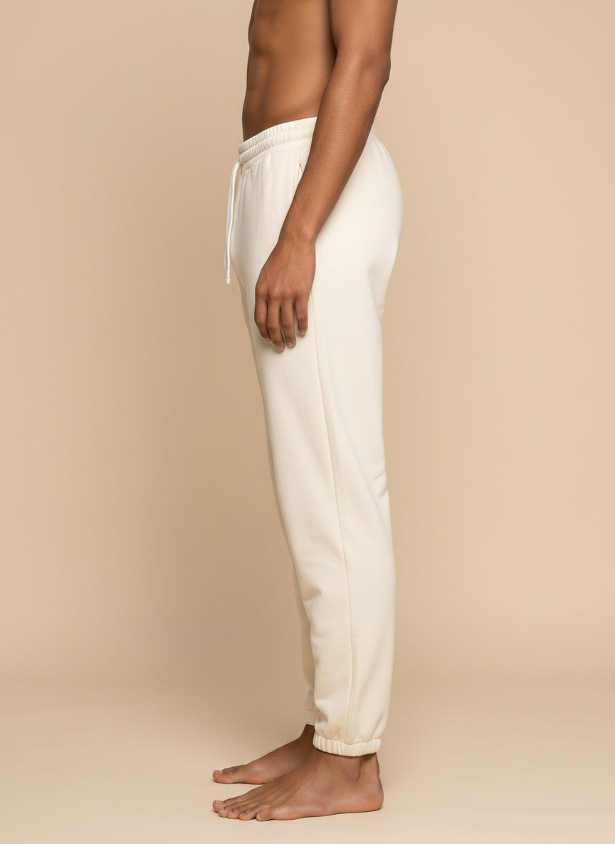 Side view of a person wearing off-white jogger sweatpants with a drawstring waistband, standing barefoot against a plain beige studio background.