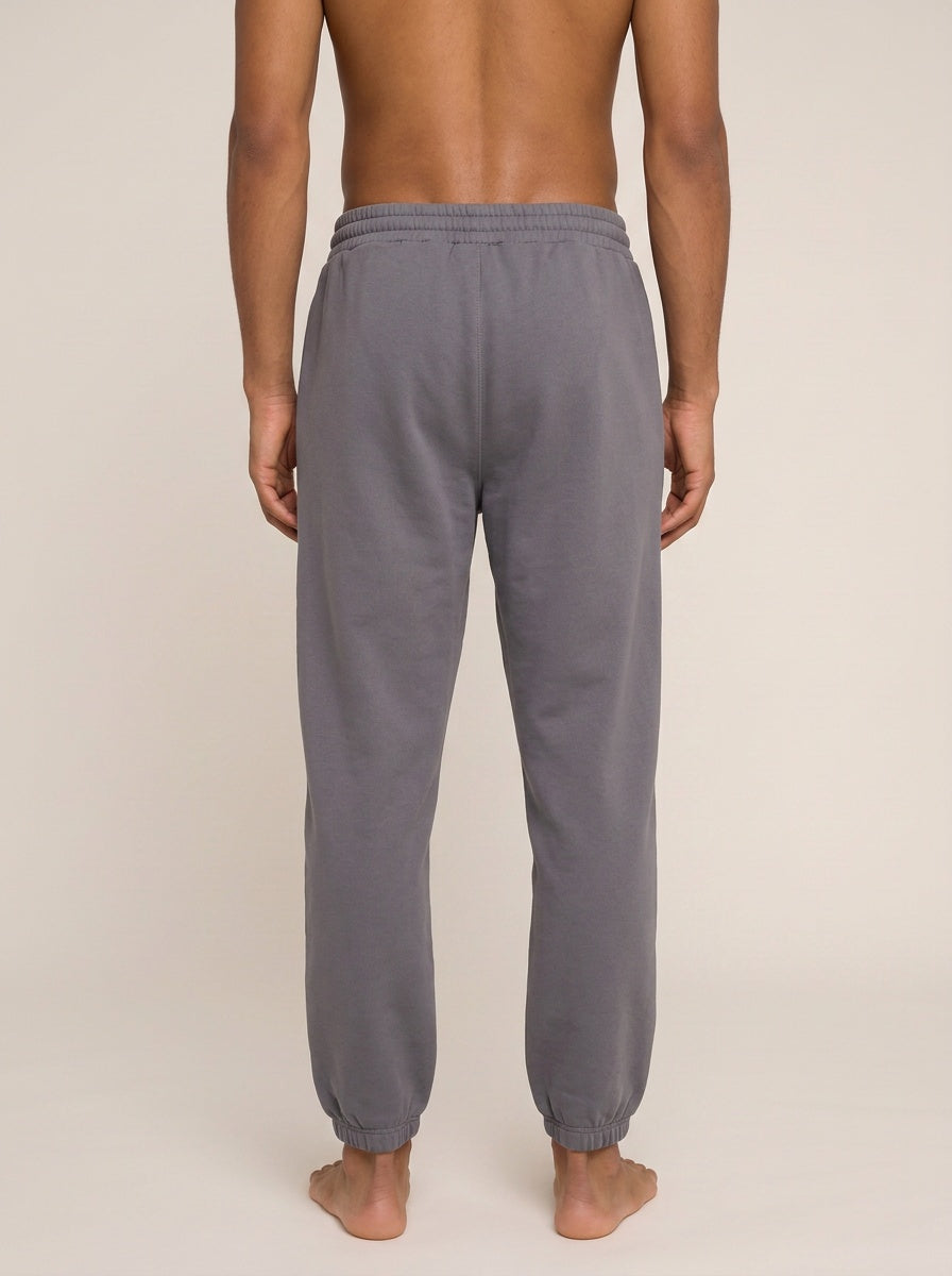 Rear view of a man wearing gray jogger sweatpants against a plain beige studio background.