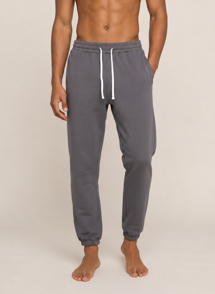 A man wearing dark gray sweatpants with a white drawstring, shown from the waist down against a plain beige studio background.