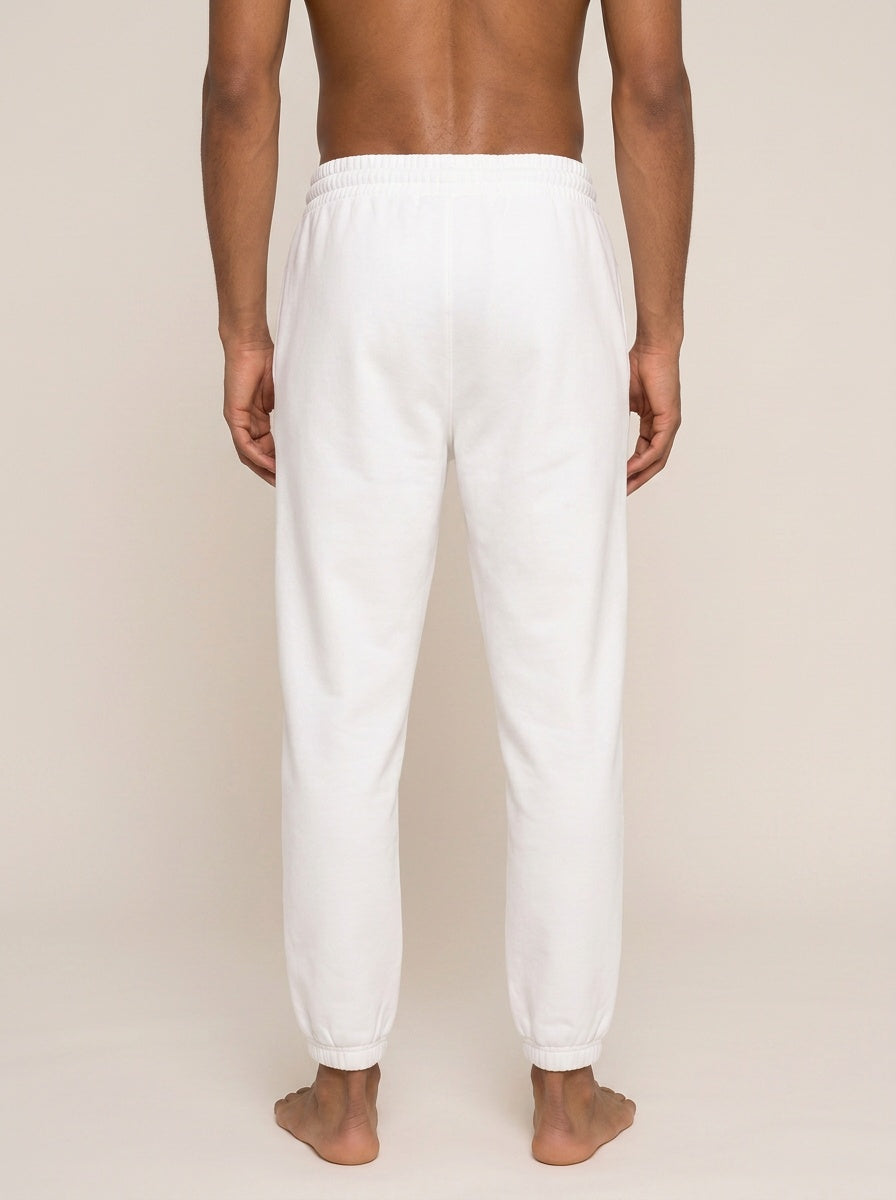 White jogger sweatpants shown from the back on a model, featuring an elastic waistband and tapered legs with elastic cuffs.