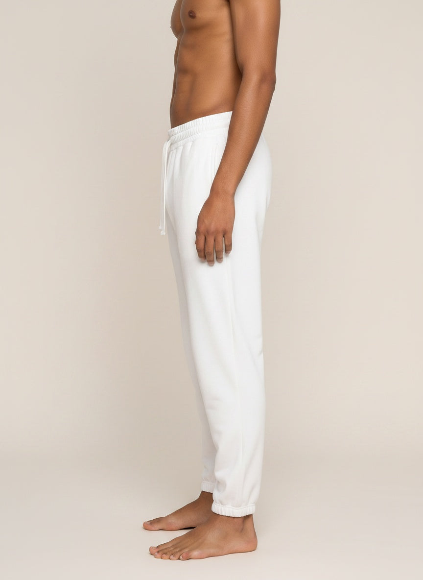 A side-profile view of a man wearing white jogger sweatpants against a plain beige studio background.