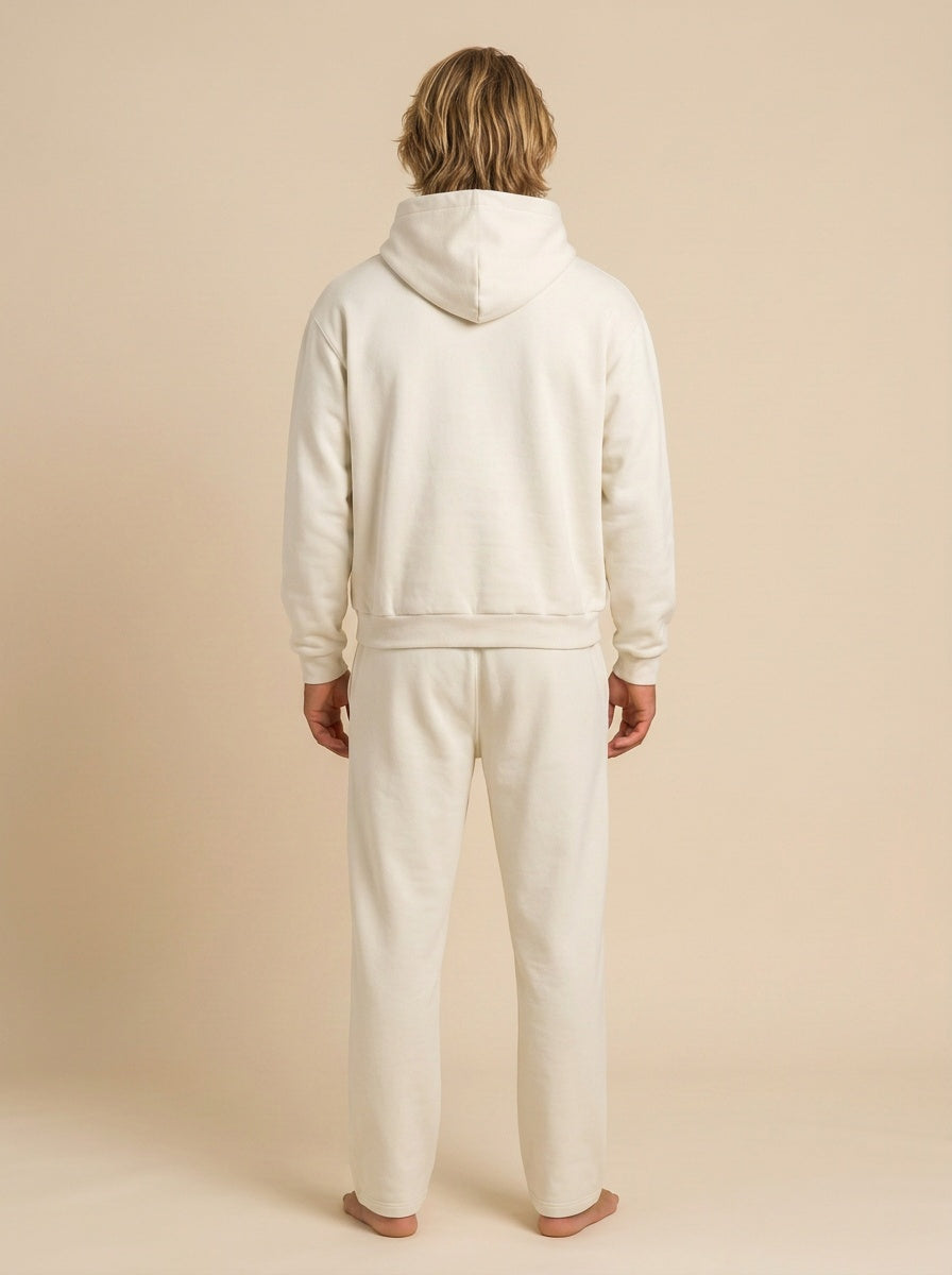 A person shown from the back wearing a matching off-white hooded sweatshirt and sweatpants set against a plain beige studio background.