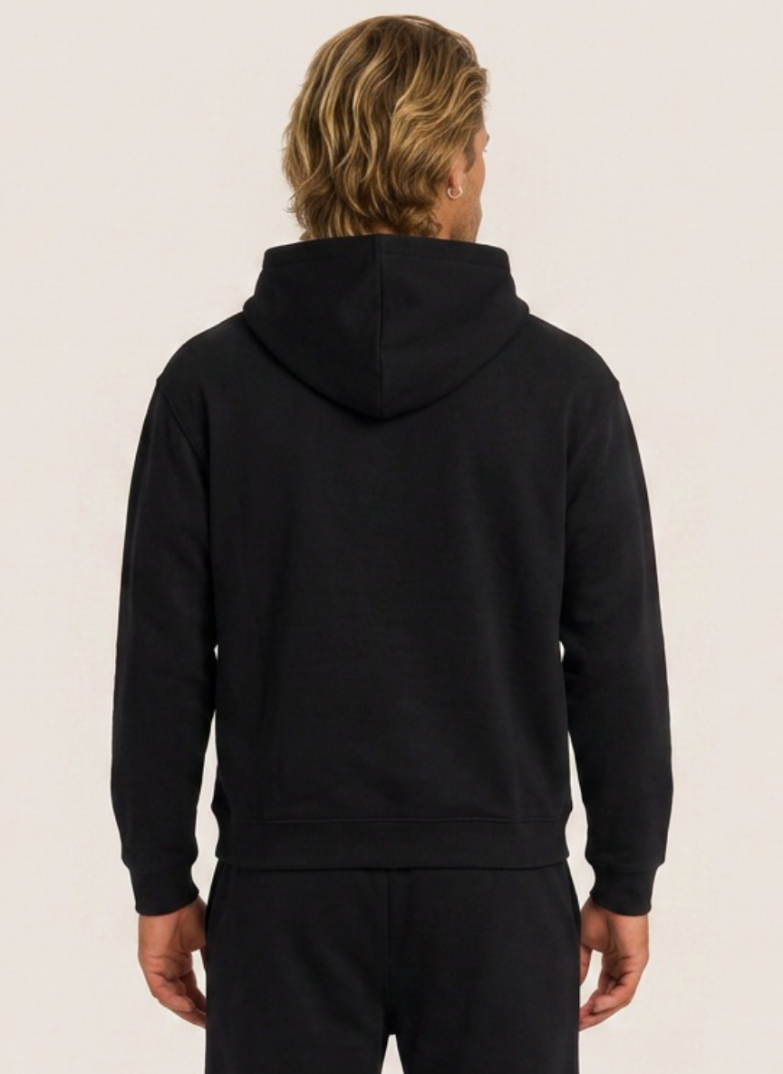 A man viewed from behind wearing a black pullover hoodie and matching black pants against a plain light background.