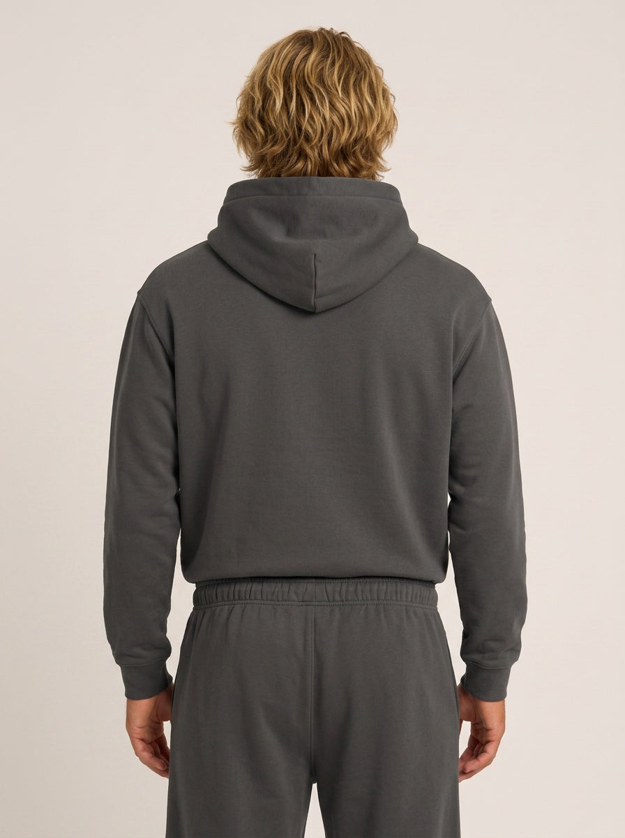 A person shown from the back wearing a dark gray hooded sweatshirt and matching dark gray sweatpants against a plain light beige studio background.