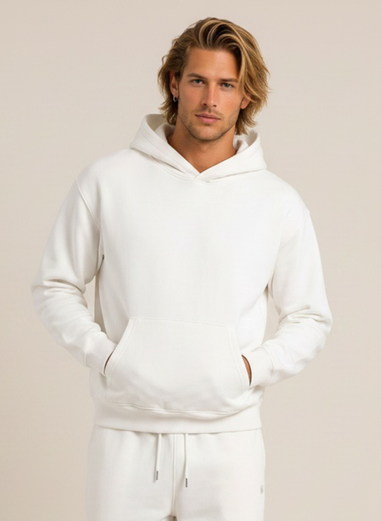 A man wearing a white pullover hoodie and matching sweatpants, standing against a plain beige studio background.