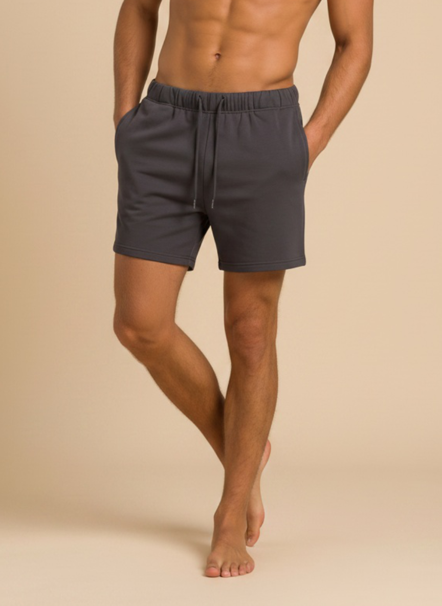 A man wearing dark gray drawstring shorts, shown from the waist down against a solid beige background.