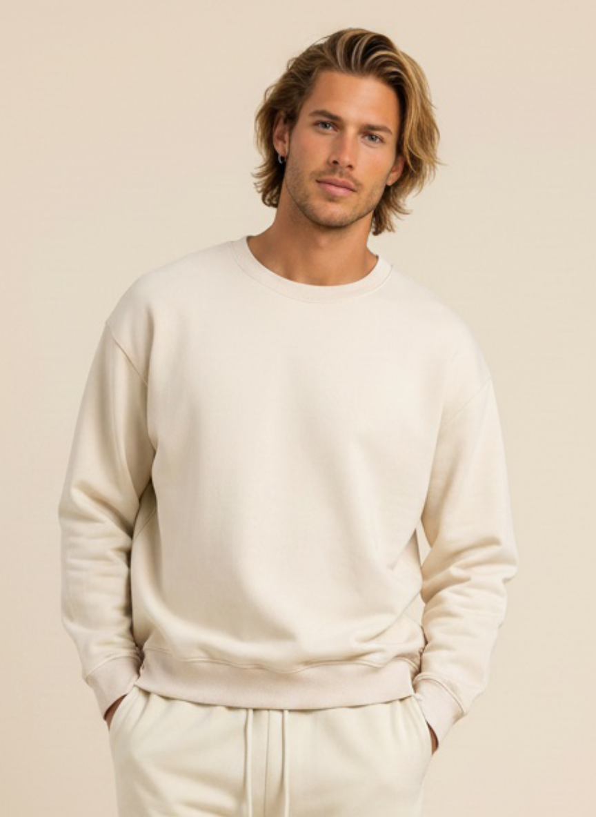 A man wearing a cream-colored crewneck sweatshirt and matching sweatpants, standing against a solid beige background.