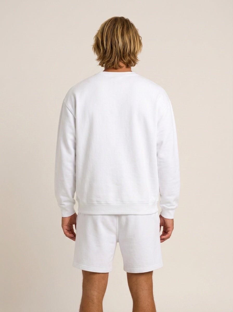 A man viewed from behind wearing a white crewneck sweatshirt and matching white shorts against a plain beige studio background.