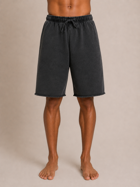 A person wearing dark charcoal gray drawstring shorts, shown from the waist down against a plain beige studio background.