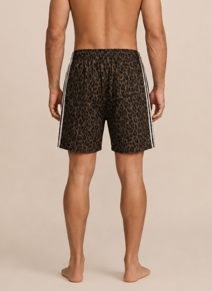 Rear view of a man wearing leopard-print athletic shorts with white side stripes, standing barefoot against a plain beige studio background.