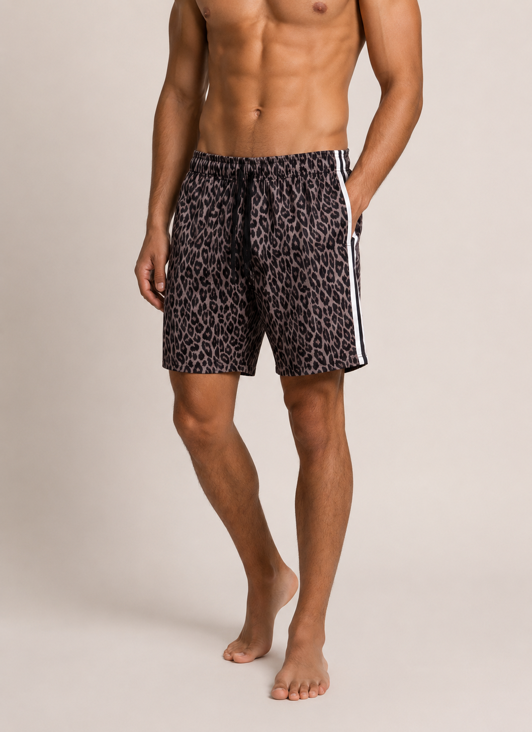 A man modeling black and brown leopard print swim shorts with white side stripes, standing against a light beige studio background.